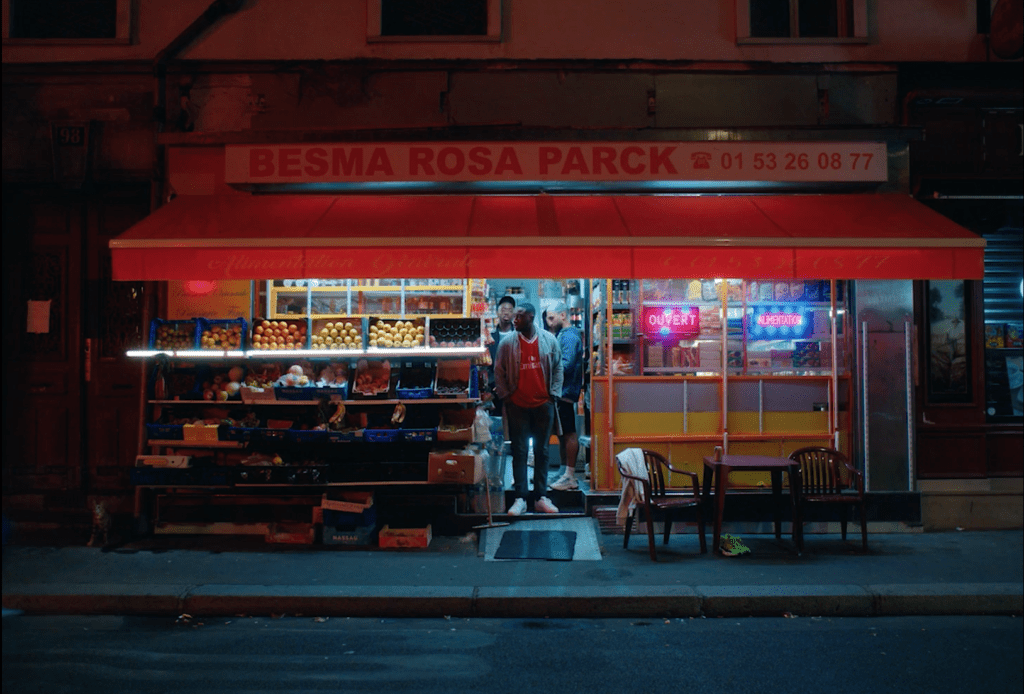 a man standing in the entrance of a nightshop, it is dark outside and the lights are on, colorfull shop