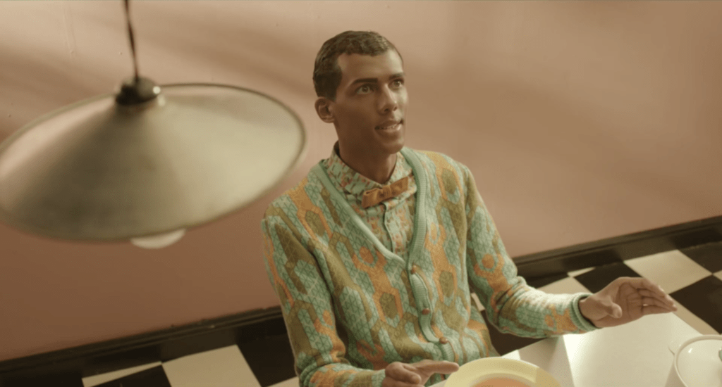 stromae the signer is sitting in a 60's interior, with clothes in paterns of the 1960's